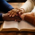 Hands joined in prayer over an open Bible